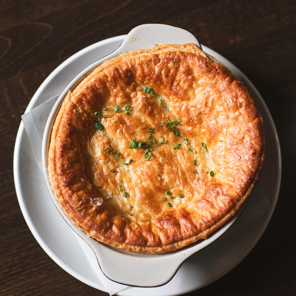 Golden-brown savory pie topped with chopped green onions, served in a white baking dish on a wooden table.