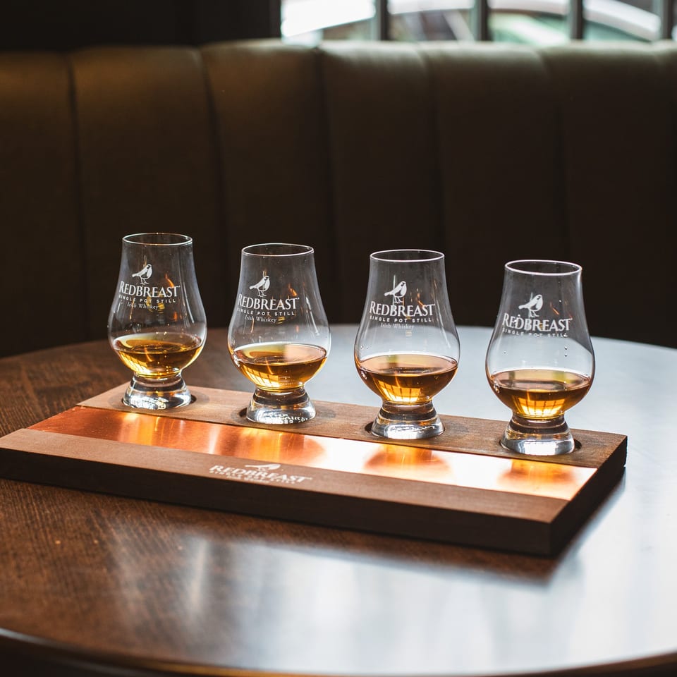 Four Redbreast Irish whiskey glasses filled with amber whiskey sit on a branded tasting tray in a restaurant booth.