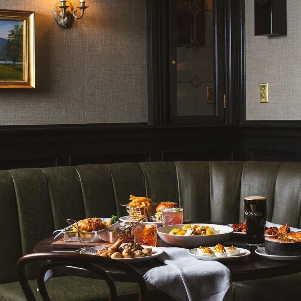 A cozy restaurant booth with a table full of various dishes, drinks, and a pint of Guinness.